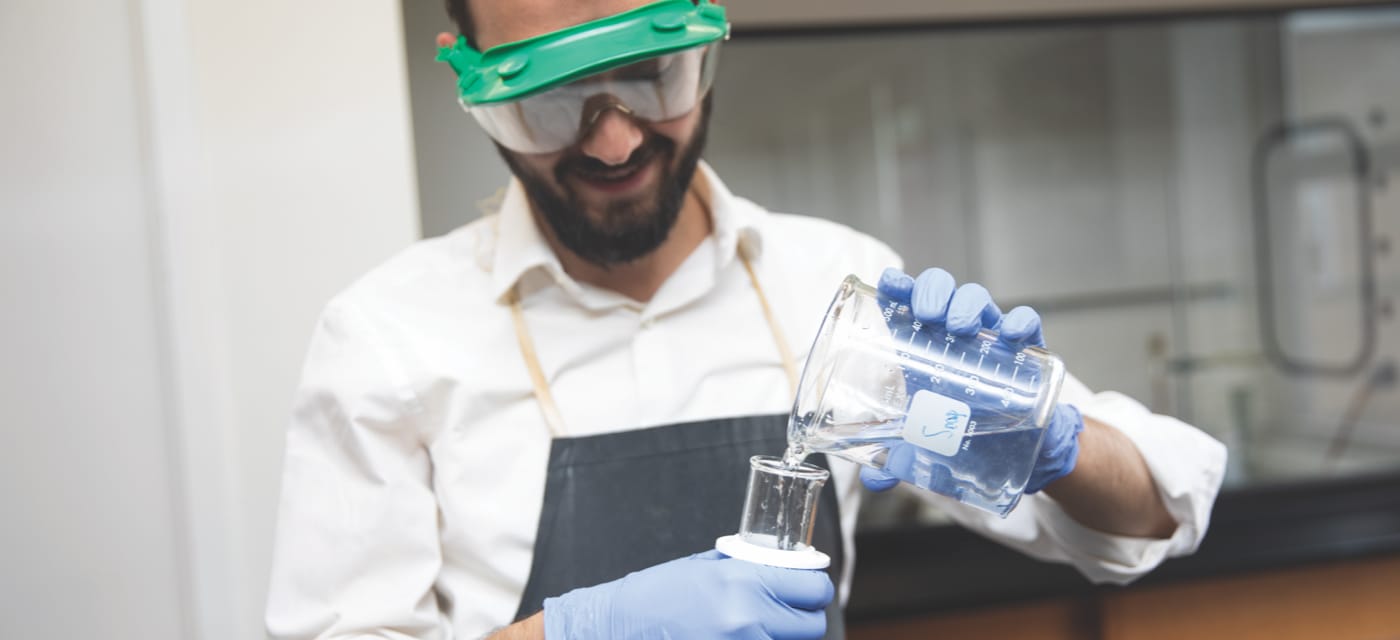 male student pouring from beaker into tube